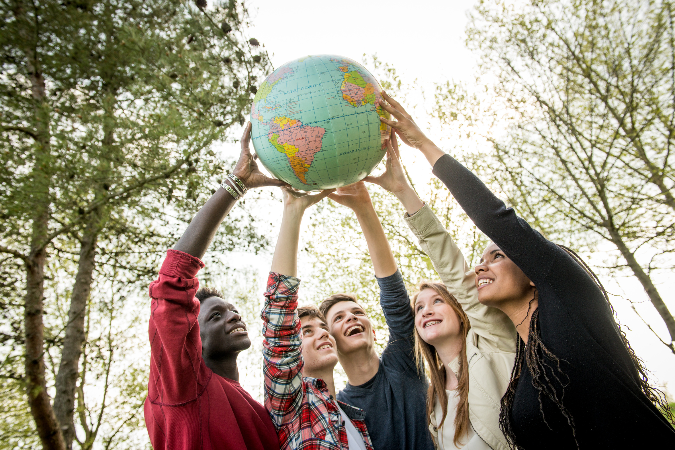 Imagen de bola del mundo cogida por las manos de jóvenes que reflejan la integración social 